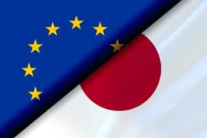Diagonal split image of the European Union flag, blue with a circle of yellow stars, and the Japanese flag, white with a central red circle. The flags intersect near the center, symbolizing a connection or relationship between the EU and Japan.