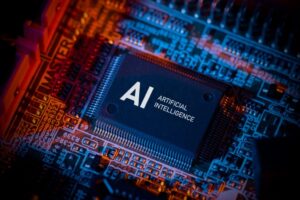 Close-up of a computer motherboard featuring a large central chip labeled "AI Artificial Intelligence." The circuit board is illuminated with blue and orange lighting, highlighting various electronic components and intricate pathways.