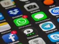 A close-up of a smartphone screen displaying various app icons. In the center, WhatsApp has two notifications, highlighted with a red badge. Surrounding apps include Dropbox, Camera, Facebook, Notes, Threema, Telegram, and Messages. The background is dark and textured.