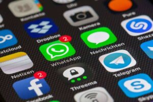 A close-up of a smartphone screen displaying various app icons. In the center, WhatsApp has two notifications, highlighted with a red badge. Surrounding apps include Dropbox, Camera, Facebook, Notes, Threema, Telegram, and Messages. The background is dark and textured.