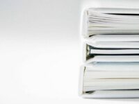 Three closed white binders are stacked horizontally against a plain white background. The binders are aligned neatly, with their spines facing right. Their pages are slightly visible and appear to be filled with documents.