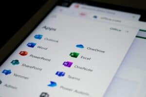 Close-up of a tablet screen displaying a list of Microsoft Office apps. Visible apps include Outlook, OneDrive, Word, Excel, PowerPoint, OneNote, SharePoint, Teams, Yammer, and Admin. Each app has its respective colorful icon next to its name. The screen has a soft blurred edge.