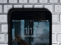 Close-up of a smartphone displaying the lock screen time as 1:17 on Friday, November 17. The phone shows 88% battery and Vodafone RO as the network. The phone is placed on a silver keyboard, with visible keys such as F5 to F9 and other special function keys.