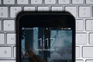 Close-up of a smartphone displaying the lock screen time as 1:17 on Friday, November 17. The phone shows 88% battery and Vodafone RO as the network. The phone is placed on a silver keyboard, with visible keys such as F5 to F9 and other special function keys.