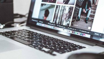 Open laptop displaying a series of photographs, featuring portraits and outdoor scenes. The keyboard is visible, and the background is slightly blurred with some equipment suggesting an office or studio setting. The screen shows images in a grid layout.